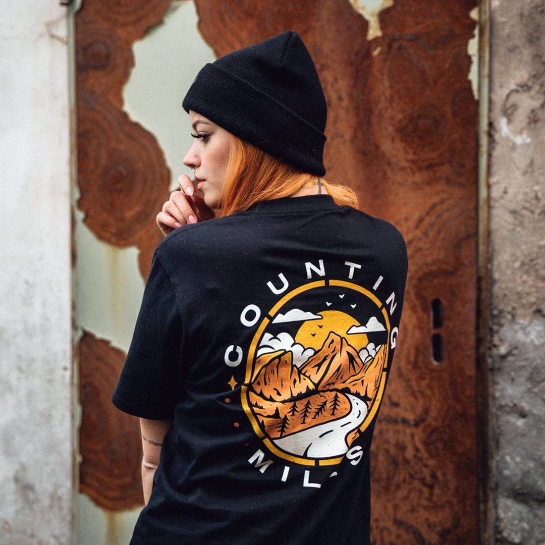 reh headed female wearing a black tshirt with a orange, yellow and white mountain scape back print