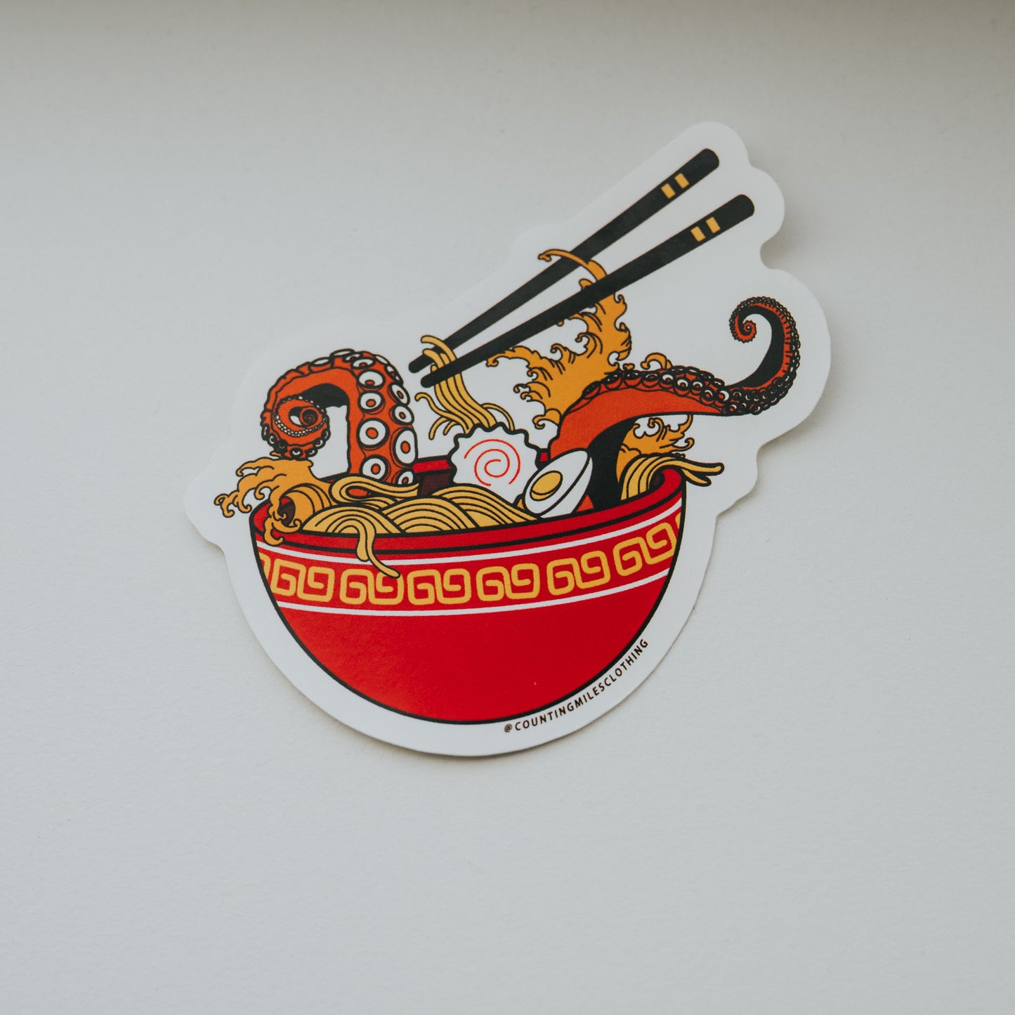 Decorative sticker with a bowl and tentacle coming out of the noodles on a white surface