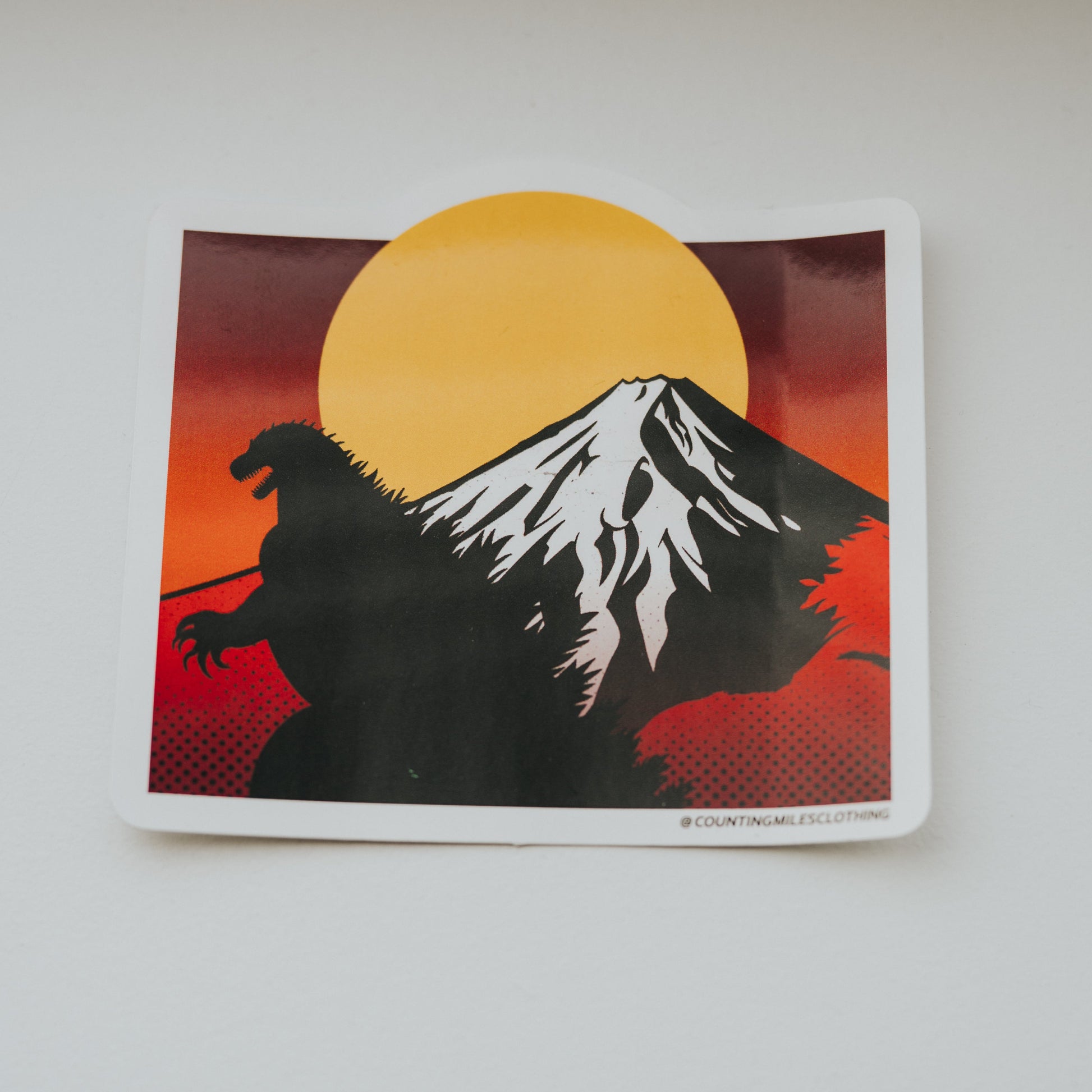 Sticker of a silhouette of a creature with a mountain and sun in the background on a white surface.