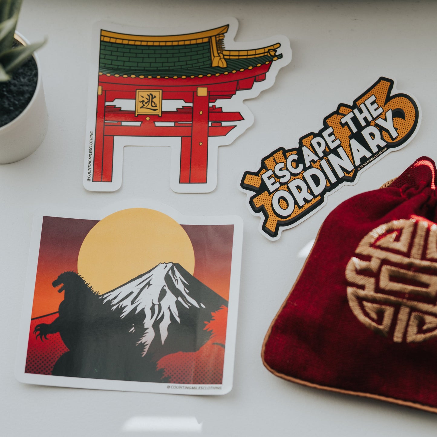 Decorative stickers on a white surface with a plant and red bag.